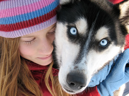 Close-up of a young girl embracing the head of a dog staring at the camera.