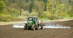 A tractor in action in a plowed field spraying chemical products. 